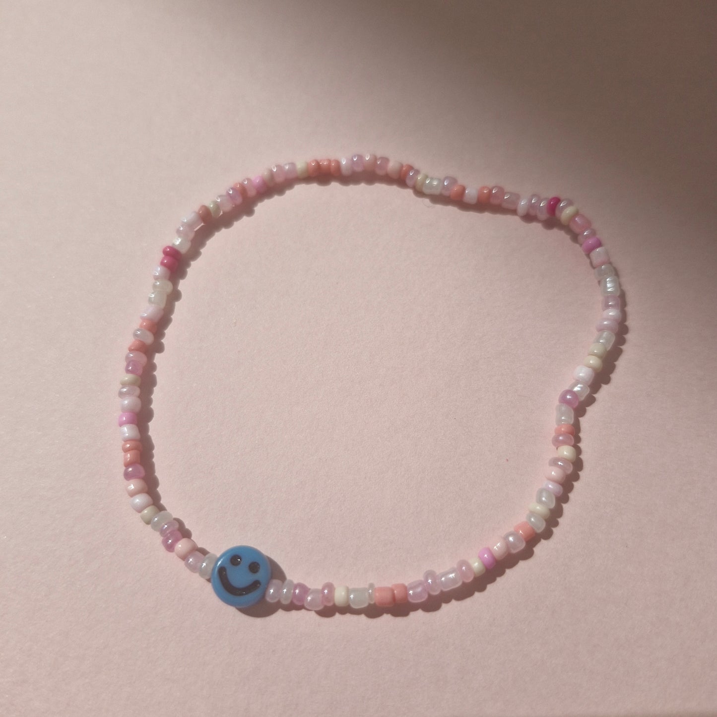 Light Pink Friendship Bracelet With A Blue Smiley Face