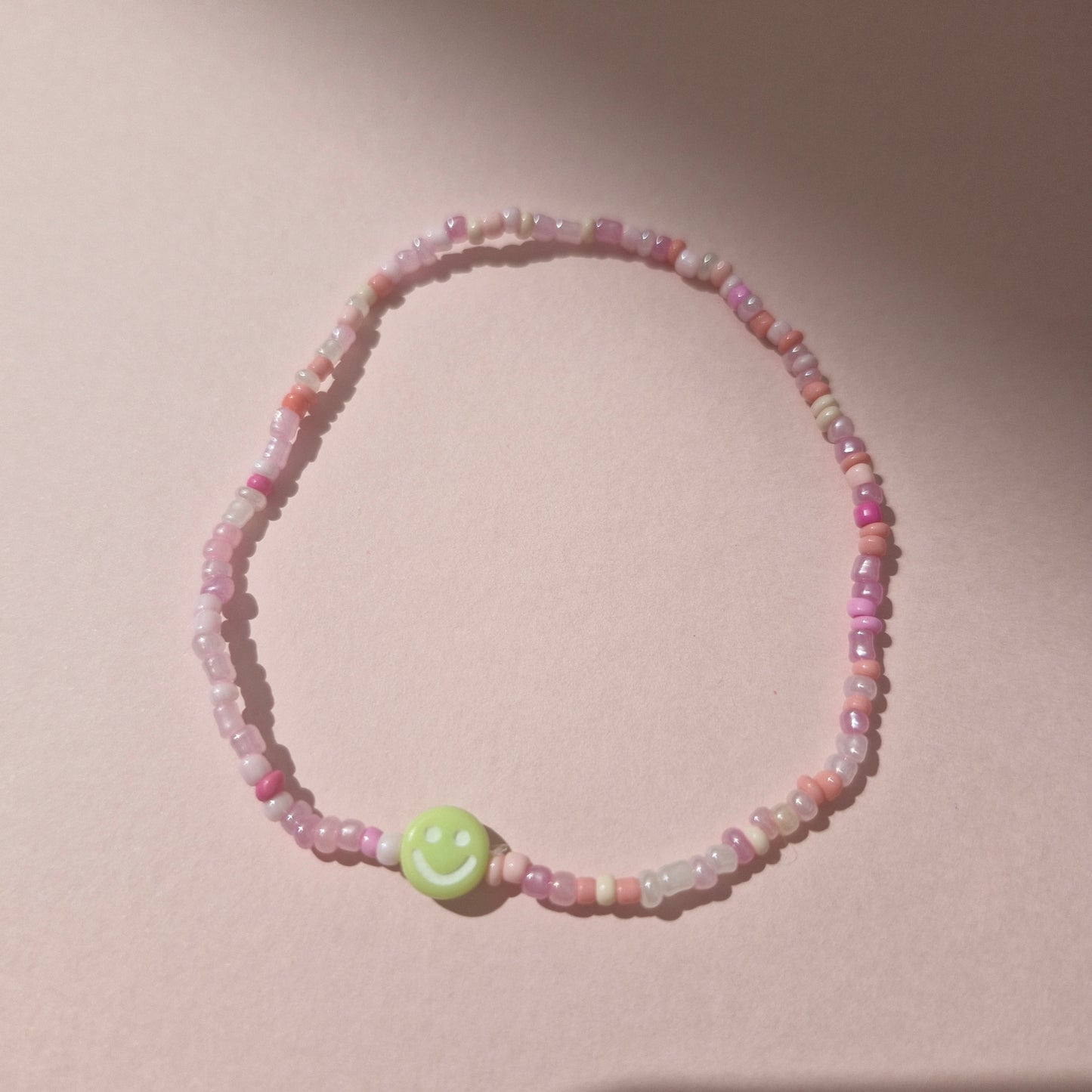 Light Pink Friendship Bracelet With A Green Smiley Face